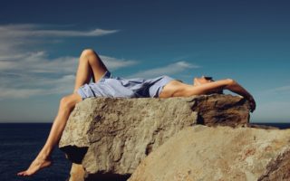 woman in blue denim shorts lying on brown rock during daytime