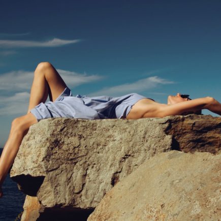 woman in blue denim shorts lying on brown rock during daytime